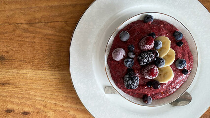 Colorful smoothie bowl topped with fresh fruits including bananas, berries, and nuts, served on a decorative plate against a wooden background