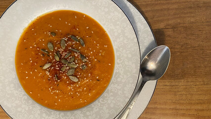Creamy orange soup garnished with seeds and spices served in an elegant bowl on a wooden table,...