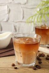 Tasty iced coffee with milk in glasses and beans on wooden table against light textured background, closeup