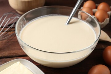 Liquid dough in bowl and ingredients on wooden table, closeup