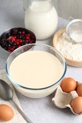 Liquid dough in bowl, berries and ingredients on light grey table, closeup