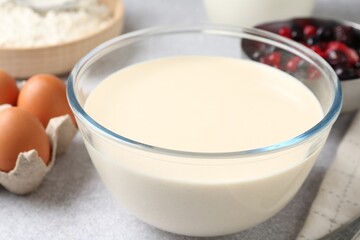 Liquid dough in bowl, berries and ingredients on light grey table, closeup