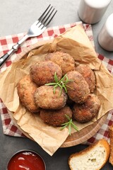 Delicious patties with rosemary in bowl, bread and ketchup served on grey textured table, flat lay