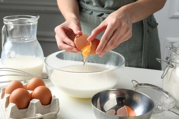Woman making batter (liquid dough) at white table indoors, closeup