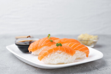 Delicious nigiri sushi with salmon, microgreens and soy sauce on grey textured table, closeup