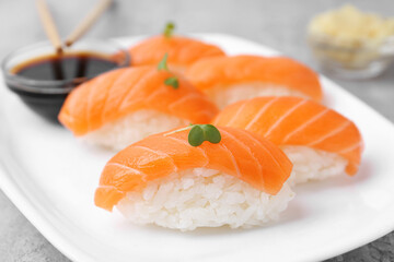 Delicious nigiri sushi with salmon, microgreens and soy sauce on grey textured table, closeup
