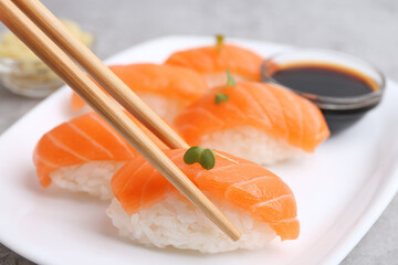 Taking tasty nigiri sushi with chopsticks at grey table, closeup