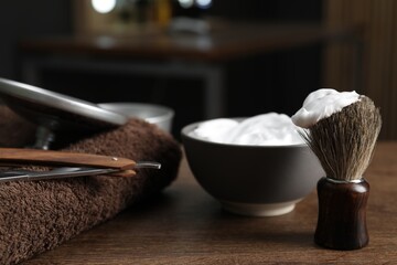 Shaving brush, foam, towel and straight razor on wooden table in barbershop, closeup