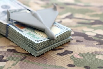 Unnamed grey toy drone and dollar bills on camouflage fabric close up. Drone manufacturing funds