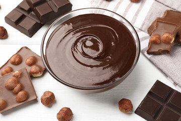 Melted chocolate and pieces with hazelnuts on white wooden table, closeup