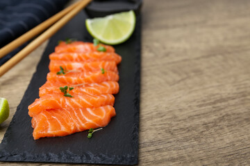 Fresh salmon sashimi with microgreens and lime on wooden table, closeup. Space for text