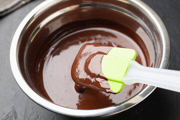 Melted chocolate and spatula in bowl on black table, closeup