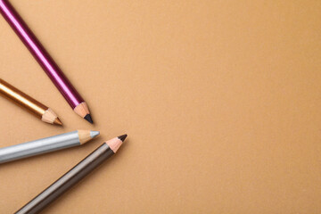 Eye pencils on brown background, flat lay. Space for text