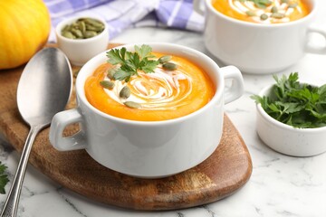 Tasty pumpkin cream soup with parsley and seeds served on white marble table, closeup