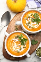 Tasty pumpkin cream soup with parsley and seeds served on white marble table, flat lay