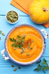 Delicious pumpkin cream soup with parsley and seeds served on blue wooden table, flat lay