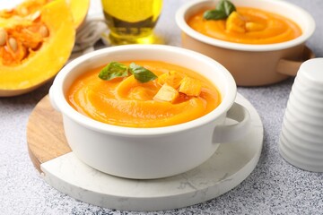 Delicious pumpkin cream soup with basil served on grey table, closeup