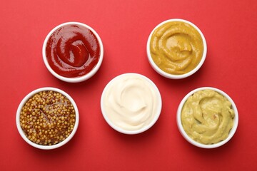 Different sauces in bowls on red background, flat lay