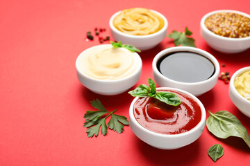 Different sauces, spices and herbs on red background, closeup