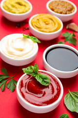 Different sauces and herbs on red background, closeup