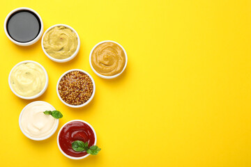 Different sauces and herbs on yellow background, flat lay. Space for text