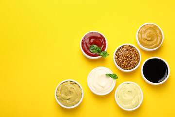 Different sauces and herbs on yellow background, flat lay. Space for text