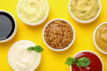 Different sauces and herbs on yellow background, flat lay