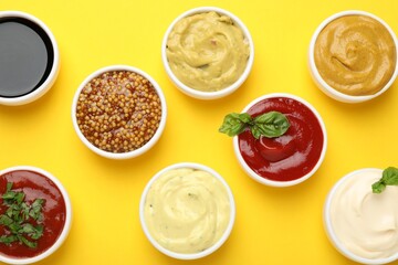 Different sauces and herbs on yellow background, flat lay