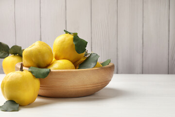 Fresh ripe quinces with leaves in bowl on white wooden table, closeup. Space for text