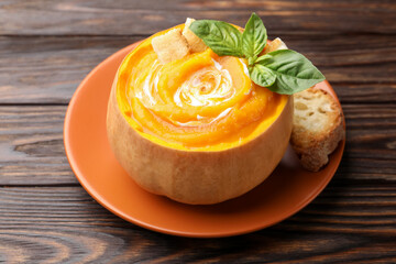 Tasty pumpkin cream soup with basil and croutons served in pumpkin on wooden table, closeup