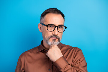 Businessman in brown shirt poses thoughtfully against a blue background symbolizing confidence and leadership