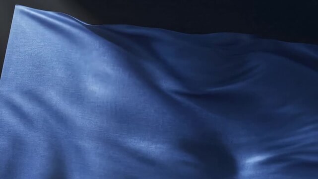 Deep blue fabric waves gently, creating soft folds and shadows in dramatic lighting.