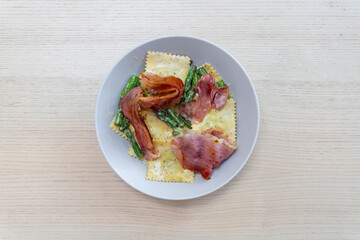 A plate of cheese ravioli with prosciutto on top.