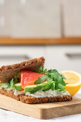 Open sandwich on whole grain bread with smoked salmon, soft cheese, avocado and arugula, healthy gourmet breakfast