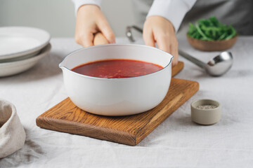 Female hands holding ladle with traditional beetroot borscht soup on linen tablecloth, rustic homemade meal
