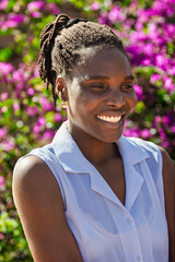 portrait , young african single with a toothy smile and braids, dreadlocks hairstyle, outdoors flowers in the background