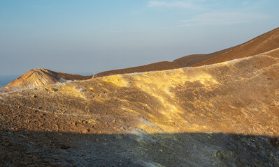 Close-up of the Fossa crater of Vulcano island with yellow sulfur deposits, steam, and volcanic rock under evening light, Sicily, Italy.