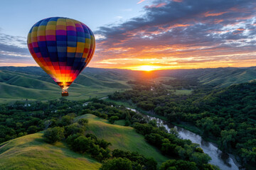 Obraz premium Colorful hot air balloon floats over lush green hills at sunrise in serene landscape