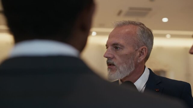 Mature Caucasian male government representative giving statement to press, surrounded by microphones, showing diplomacy and professional communication