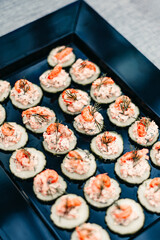 Close-up of delicate salmon and cream appetizers on cucumber slices, arranged neatly on a dark serving tray. Elegant presentation for cocktail party or catering concept.
