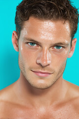 Obraz premium Close up portrait of young man with fresh youthful skin, wet face, blue eyes, and short brown hair against turquoise background, confident and relaxed expression