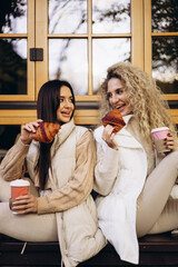Two women drinking coffee and eating delicious croissant and sitting outside the cafe