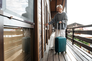 A young, stylish woman with a suitcase opens the door to a house. It's a trip or a business trip....