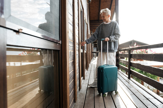 A young, stylish woman with a suitcase opens the door to a house. It's a trip or a business trip. Wooden floors and handrails.