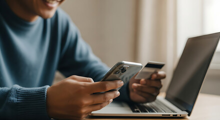 Man using phone and credit card for online shopping and payment on laptop