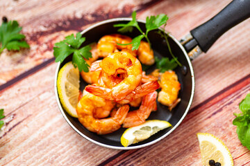 Delicious sea shrimps with lemon and butter in a frying pan on a wooden