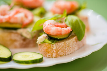Isolated mini canapes with shrimps, lettuce and cucumber, on a green background