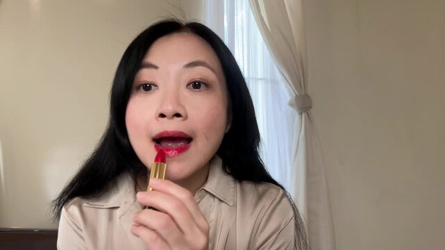 footage of Chinese Asian woman applying red lipstick. Depicting daily makeup routine, getting ready to go out. 