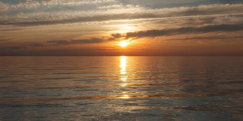 Fototapeta premium Serene sunset paints the calm ocean with vibrant golden light reflecting on tranquil waters