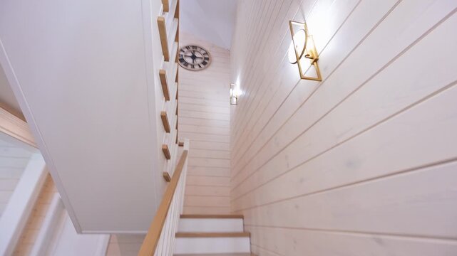 A bright, modern staircase with white risers and wooden treads ascends against a light wood-paneled wall, accented by elegant gold lighting